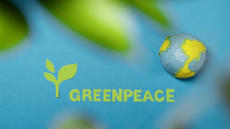 Greenpeace logo and Earth cutout on blue background symbolizing environmental awareness. Greenpeace logo and Earth cutout on blue background symbolizing environmental awareness.