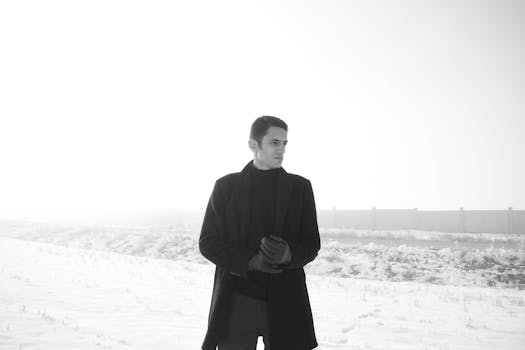 A man in black attire stands in a snowy outdoor setting, creating a striking contrast.