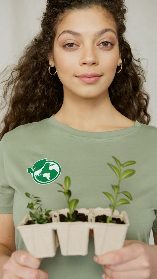 Free A Woman in Green Shirt Holding Boxes of Young Plants Stock Photo