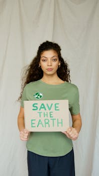 A young woman in a green shirt holds a 'Save the Earth' sign promoting environmental activism.