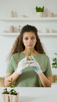 A young woman tending to plants indoors, wearing gloves and a green shirt, emphasizing plant care.