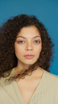 Close-up portrait of a woman with curly hair against a vibrant blue background.