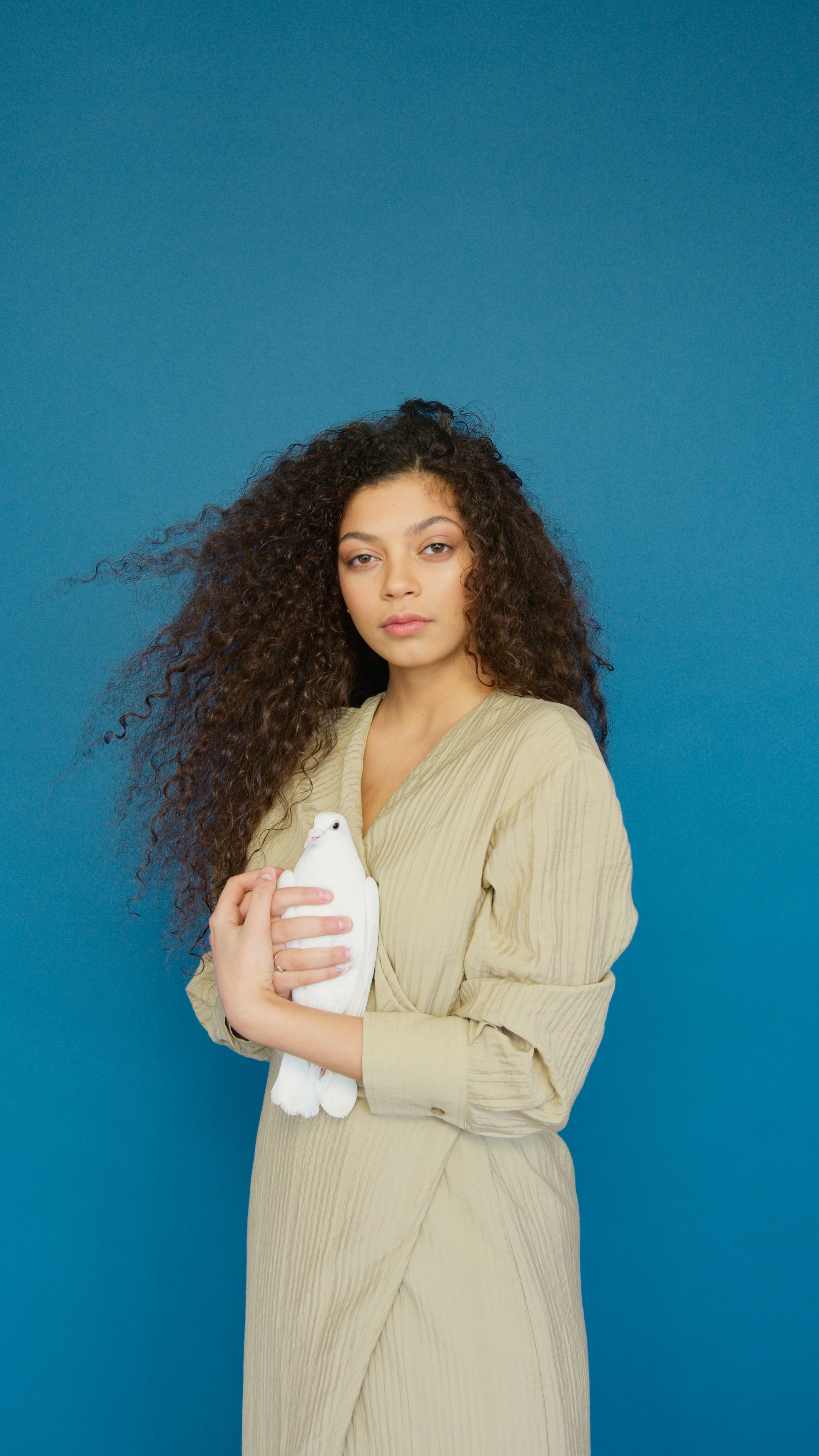 A woman gracefully holds a dove against a vivid blue background, symbolizing peace and serenity.