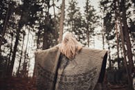 一位金发女子披着图案披肩，坐在宁静的森林中