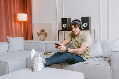 Free Man in Brown Crew Neck T-shirt and Blue Denim Jeans Sitting on White Couch Stock Photo