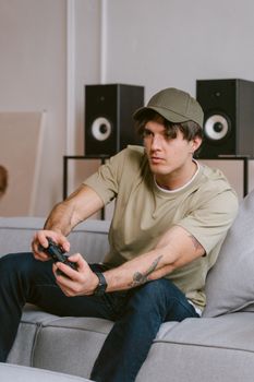 Tattooed man sitting on a couch, intensely focused on video gaming.