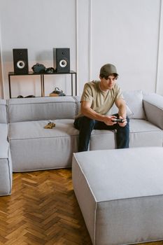 A young man plays video games on a couch in a modern living room, enjoying leisure time.