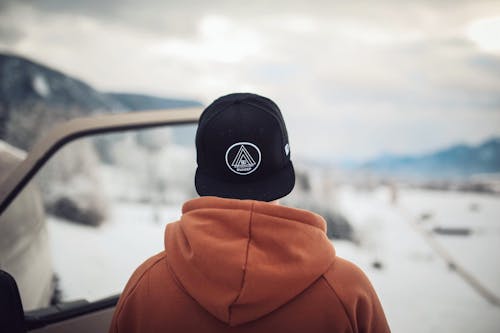 Person Wearing Black Cap and Orange Hoodie Turning His Back