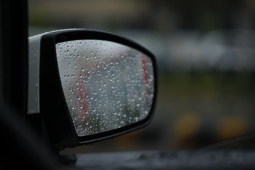 Close-up of a car's side mirror with raindrops, creating a blurred reflection effect.
