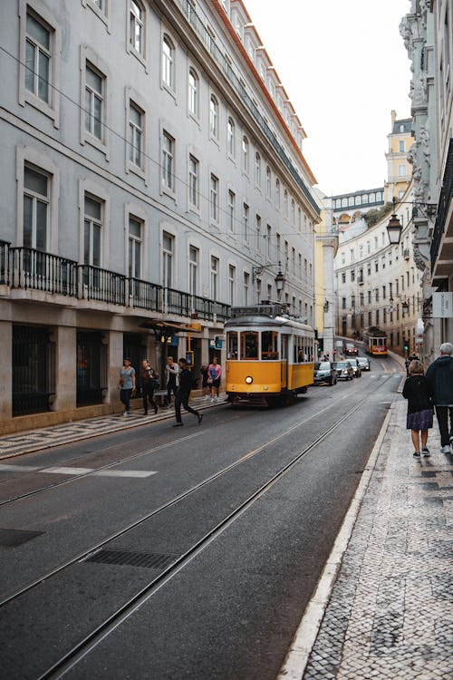People Walking Near a Yellow Tram Between Buildings