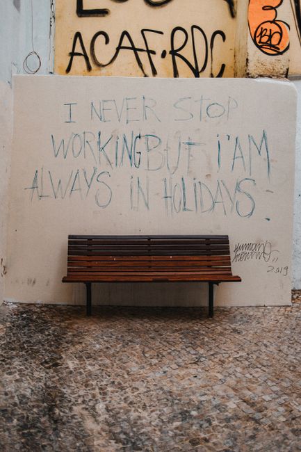 Wooden bench against a graffiti-covered concrete wall with text in an urban setting in Portugal.