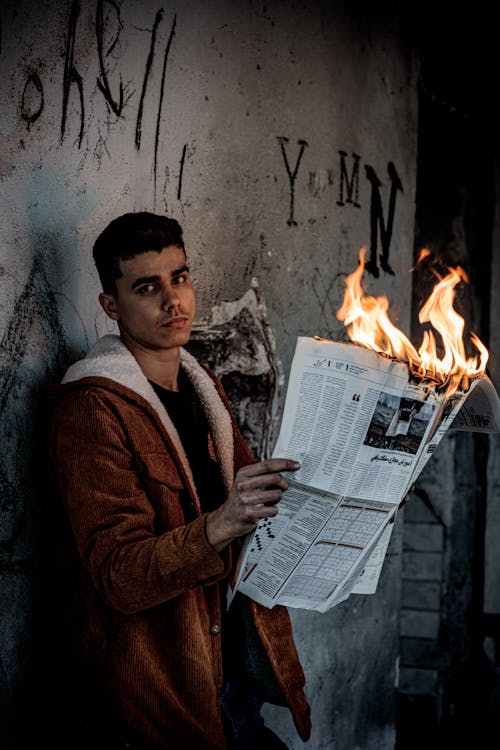 Man in a Brown Coat Holding a Burning Newspaper