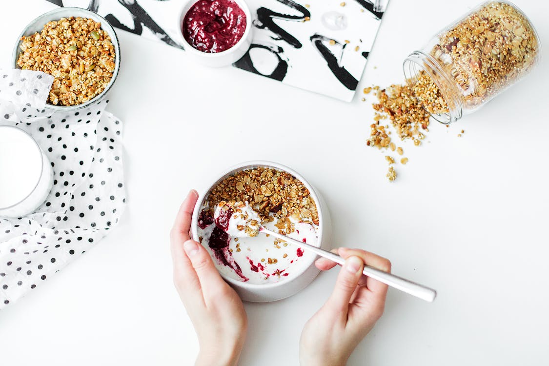 Person Mixing Cereal, Milk, and Strawberry Jam on White Ceramic Bowl