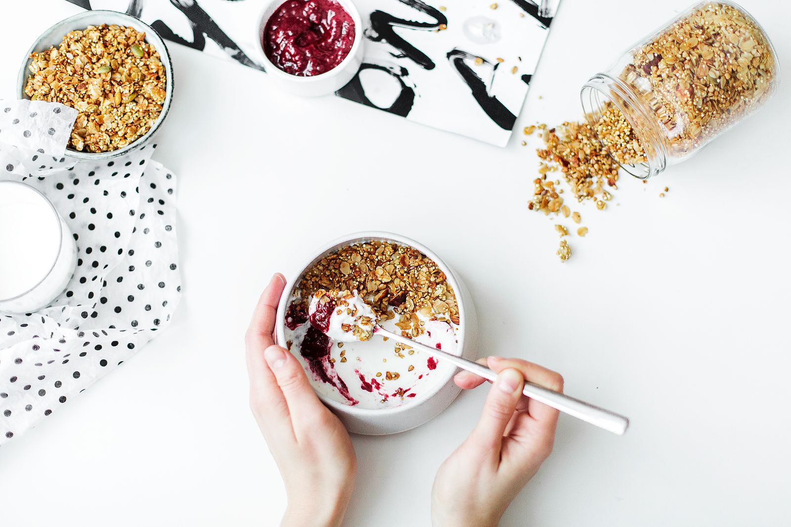 A woman's hands eating a breakfast bowl of yogurt, granola, and berries at a table