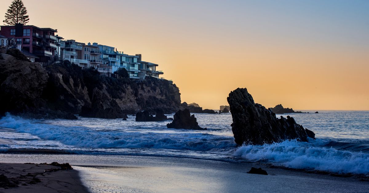 Stunning sunset over Newport Beach, CA with waves crashing against the rocky shoreline.