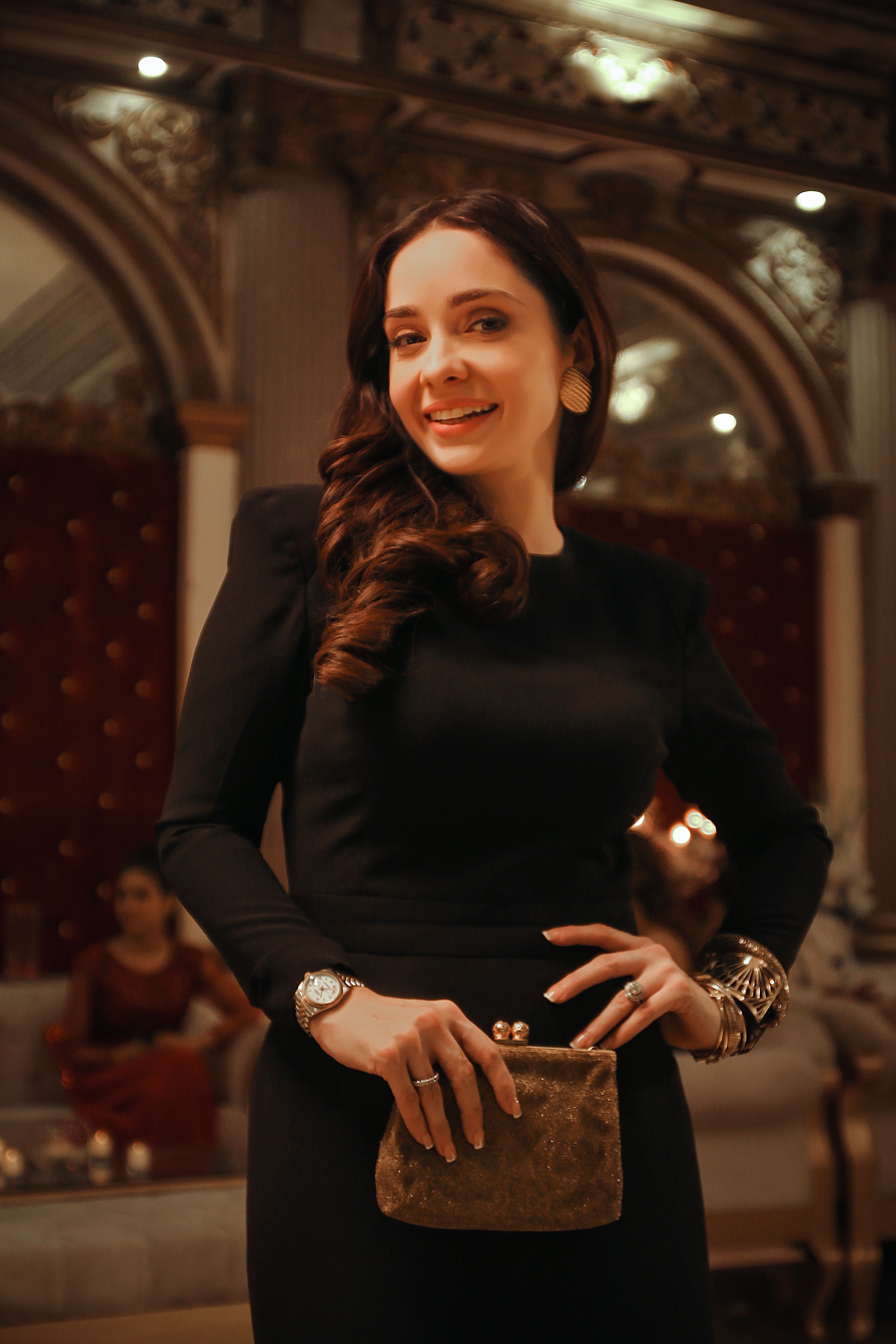 Elegant woman in black dress posing with a smile indoors.