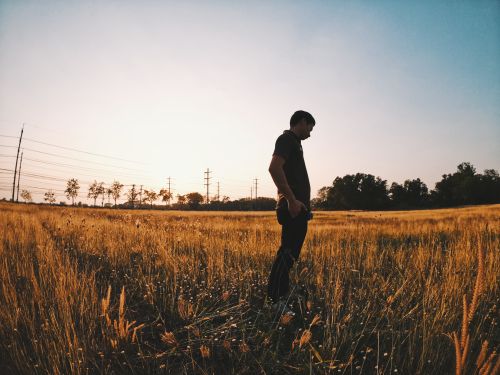 Free Silhouette of a man standing in a sunlit field during sunset, creating a peaceful scene. Stock Photo