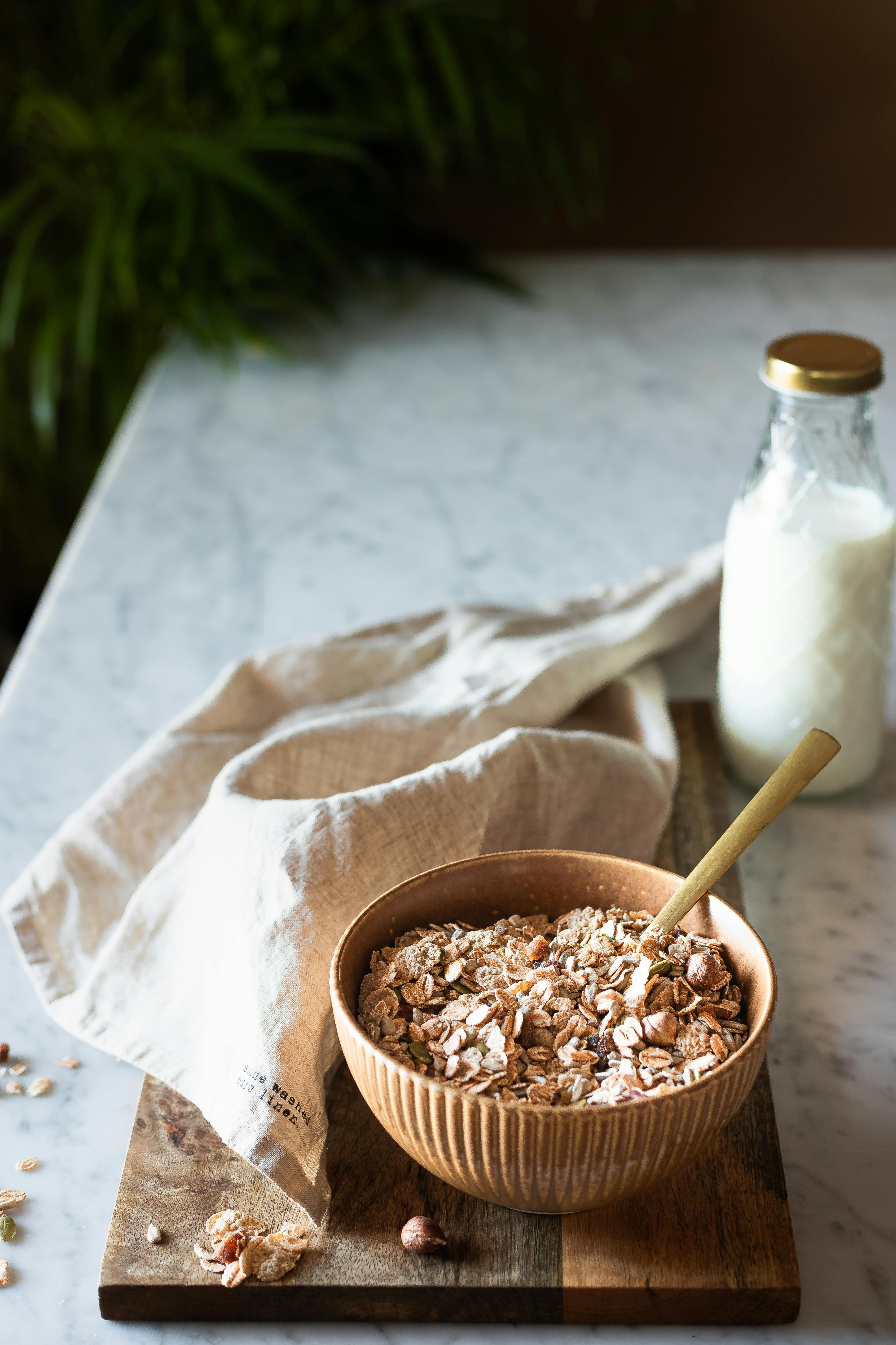 A cozy breakfast setup with cereal in a wooden bowl and a bottle of milk on a marble countertop.