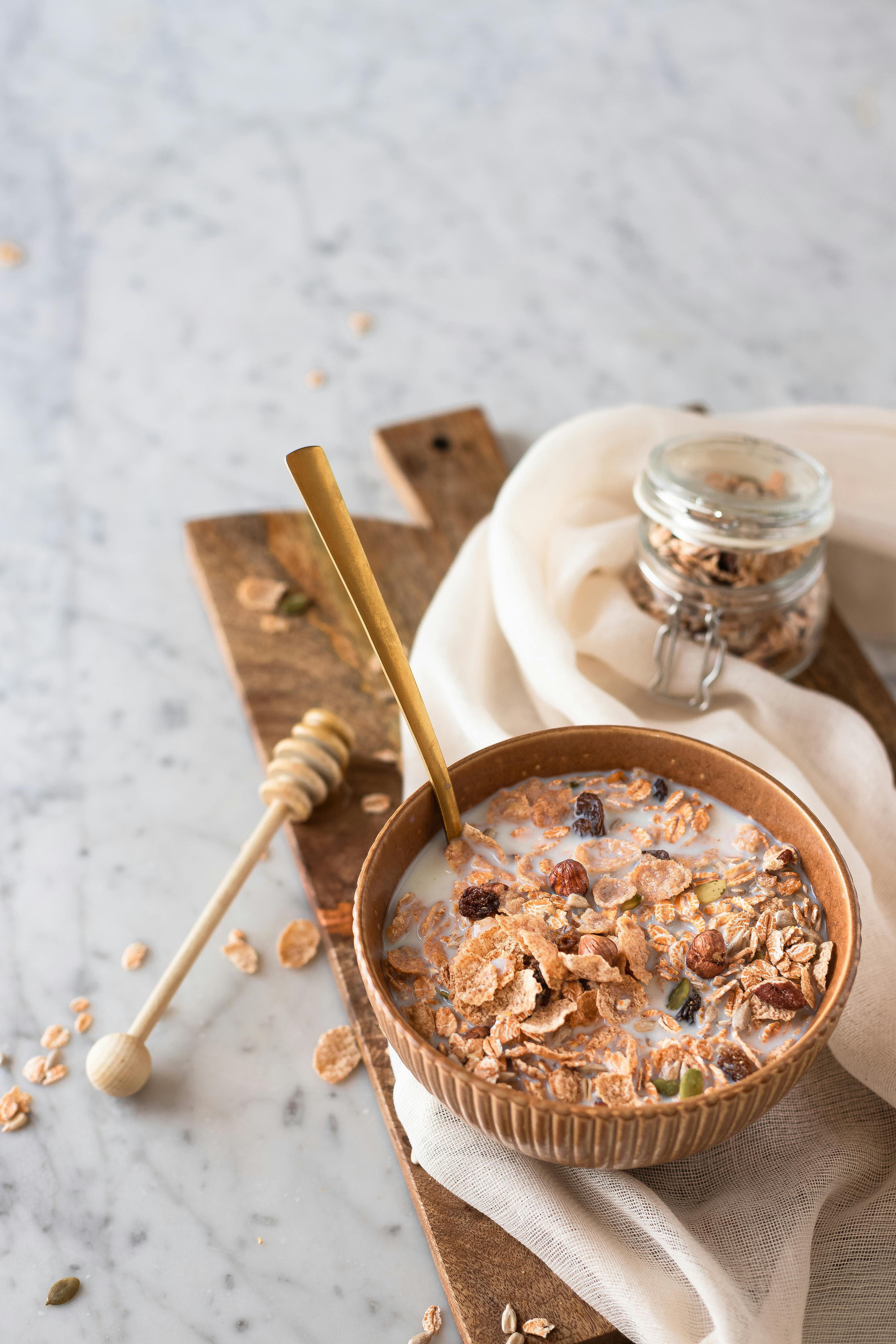 Delicious bowl of cereal with milk, granola, and honey on a wooden board.