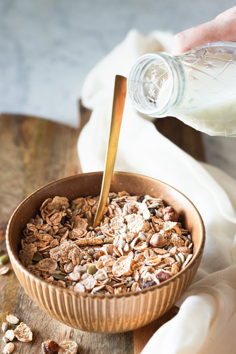 Person Holding A Bottle Of Milk Near Cereal Bowl