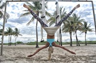 一位金发女子在棕榈树环绕的沙滩上表演空中瑜伽