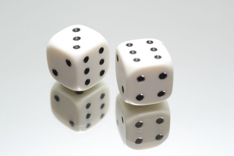 A close-up view of two white dice with reflection on a smooth white surface, symbolizing luck and chance.