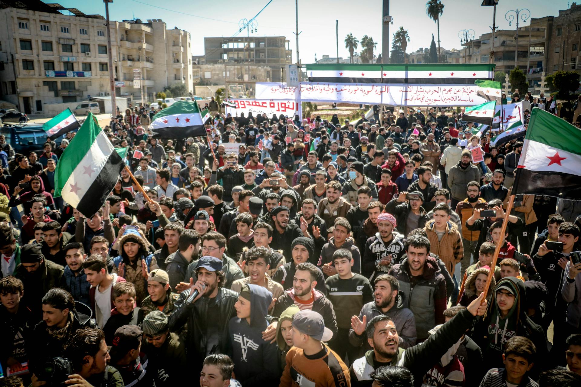 A large group of protesters rally in Idlib, Syria, raising Syrian flags and banners.