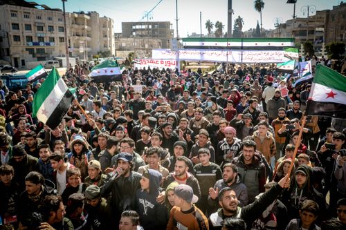 Free A large group of protesters rally in Idlib, Syria, raising Syrian flags and banners. Stock Photo