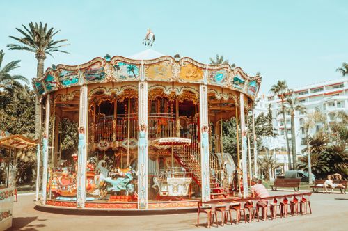 Free A colorful vintage carousel in a sunny amusement park with palm trees and vibrant decorations. Stock Photo