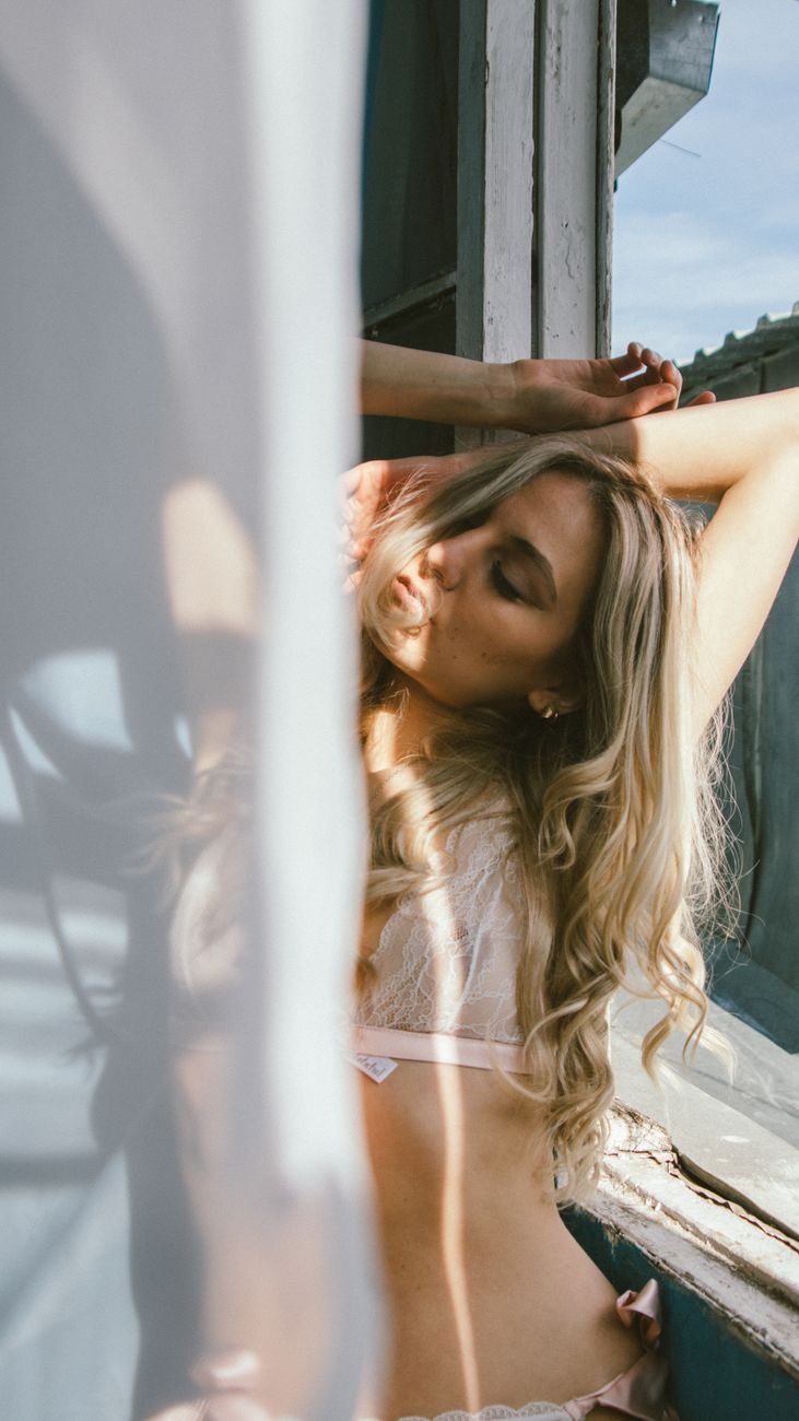 A serene portrait of a woman in lingerie, basking in warm sunlight by a window.