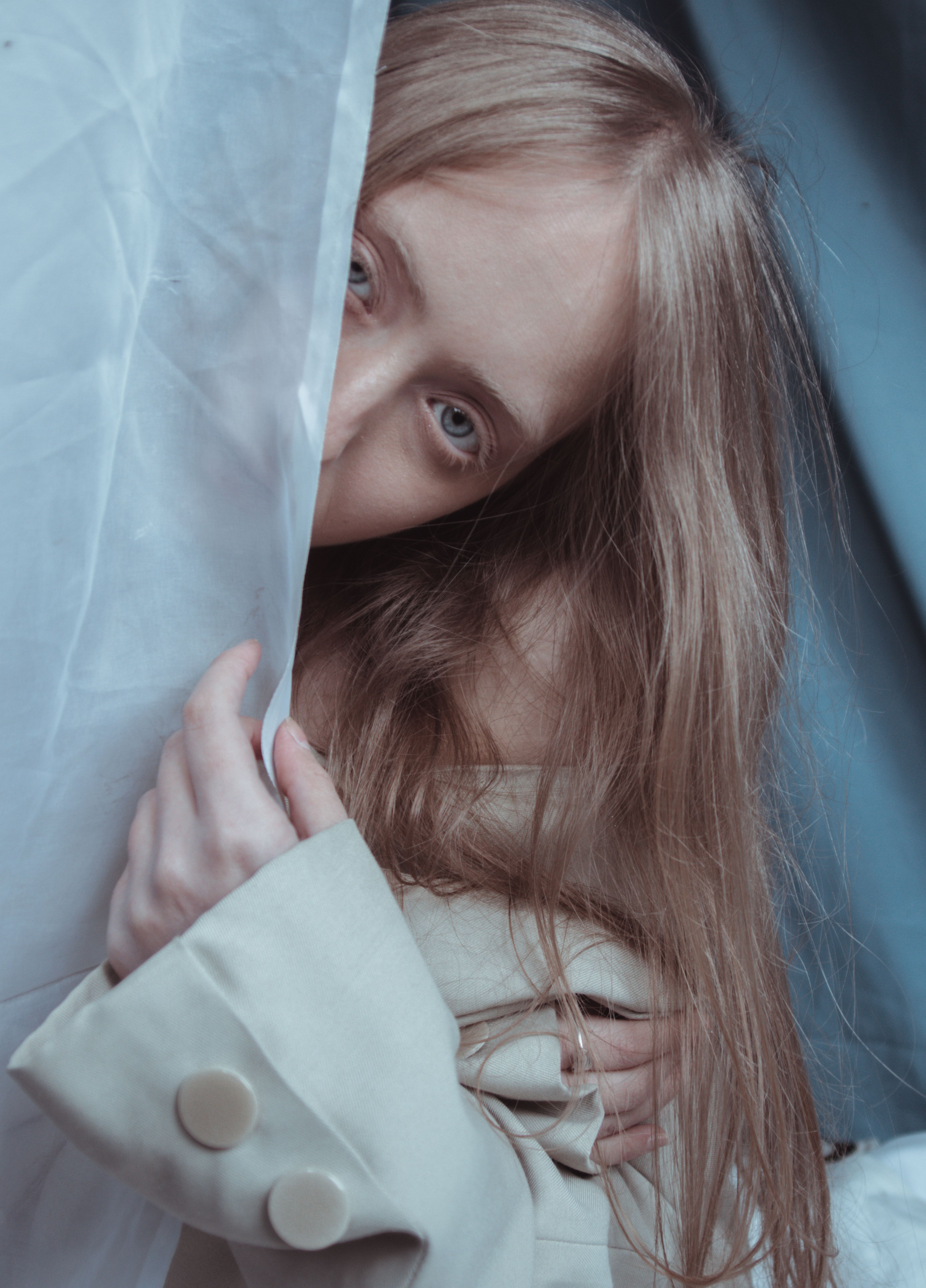 A woman gazes introspectively, partly covered by sheer fabric, creating a moody ambiance.