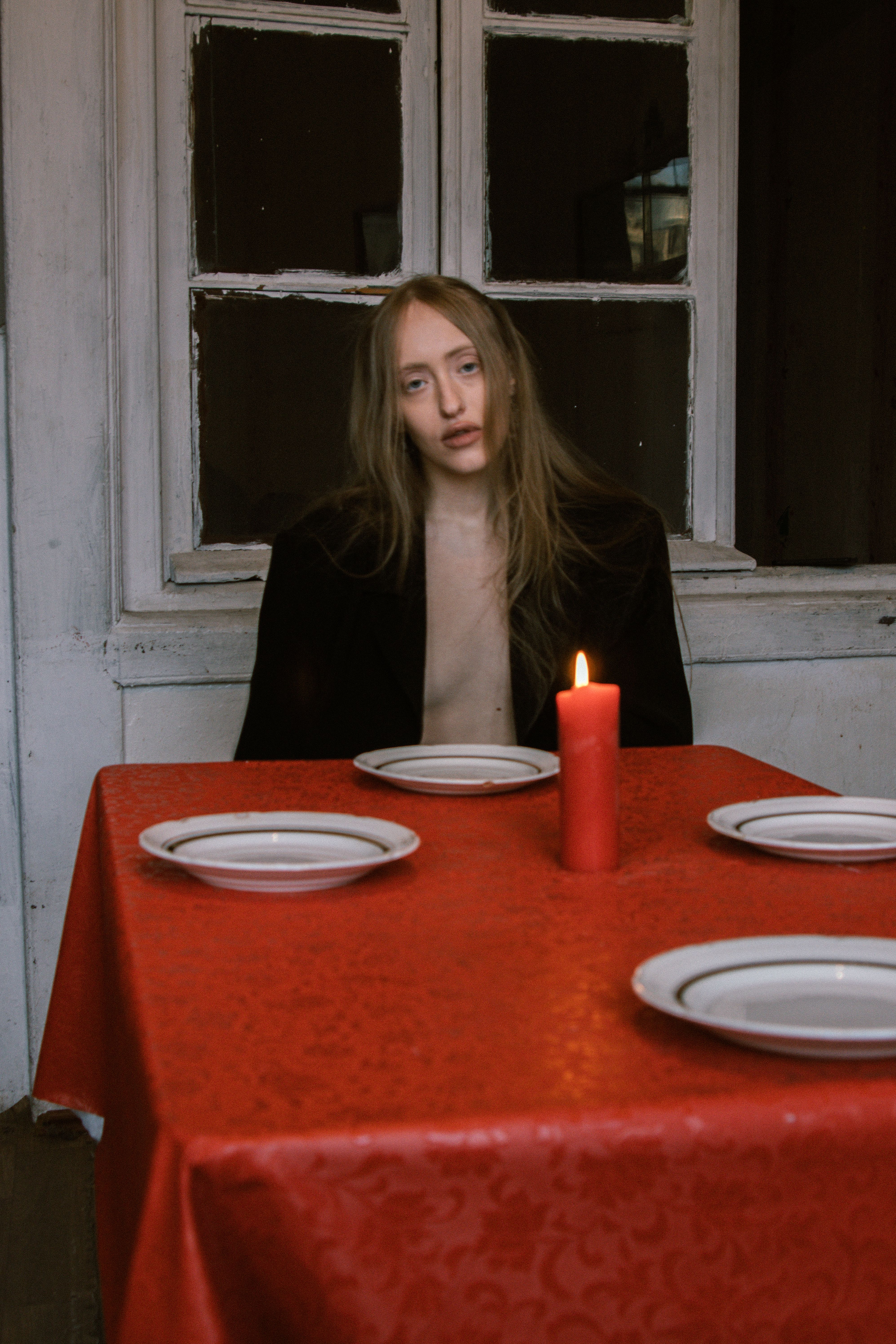 A woman with long hair sits at a table set with plates and a candle.