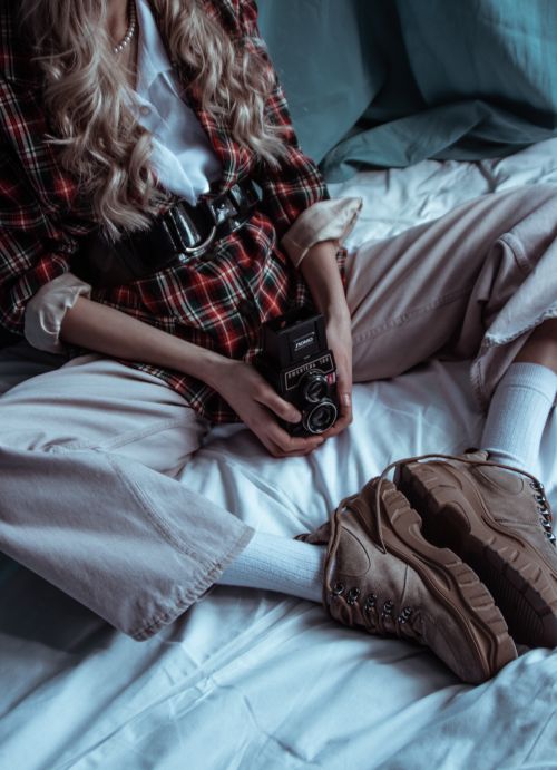 Free A fashionable woman with blonde hair sits on a bed holding a vintage camera. Stock Photo