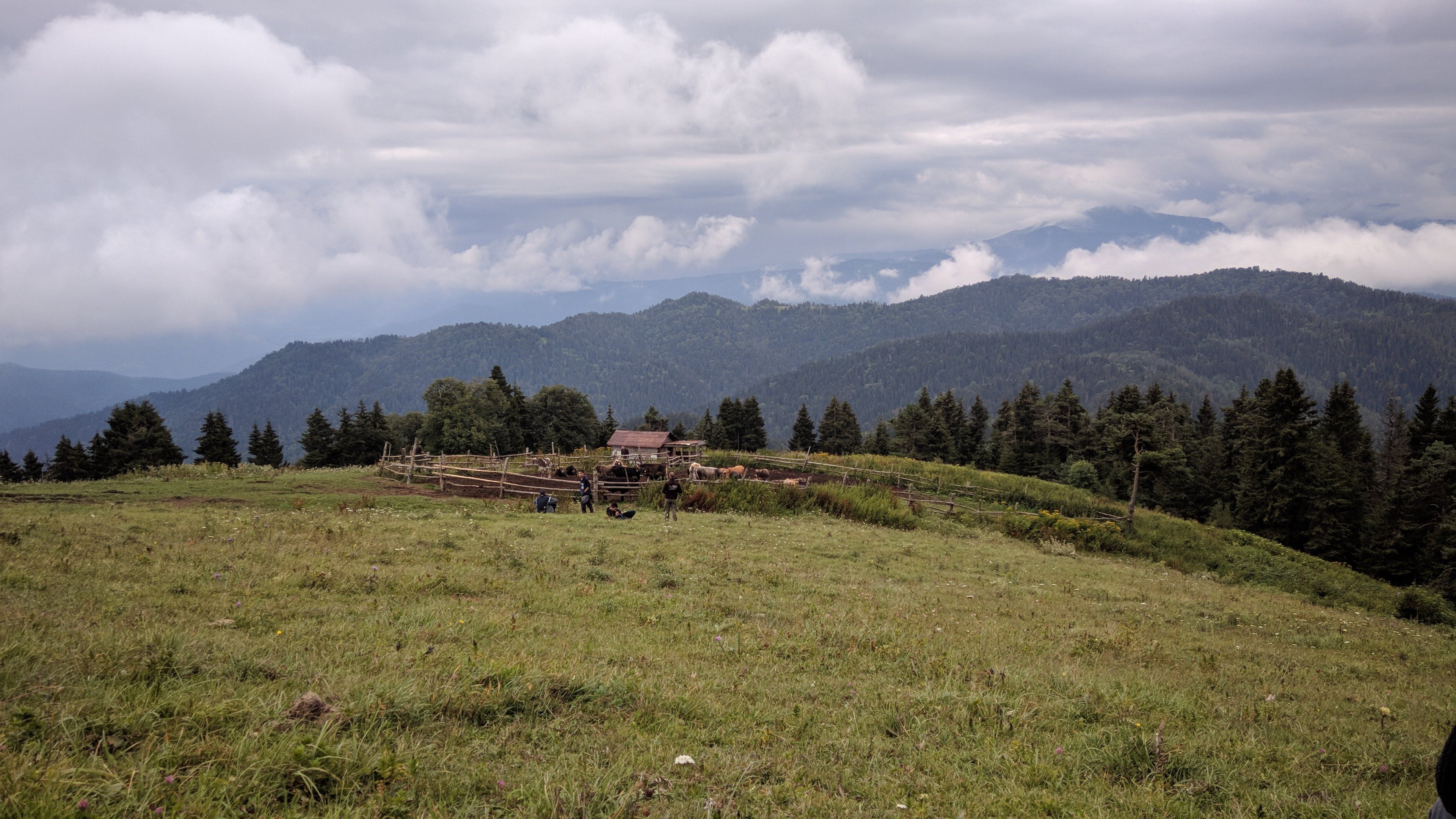A tranquil scene of a rustic farm nestled in rolling mountains under cloudy skies.