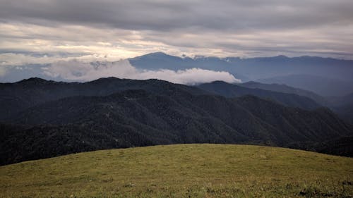 Green Grass Field and Mountains Under White Clouds