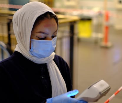 Female healthcare worker in a mask and hijab checking temperature in a clinic.