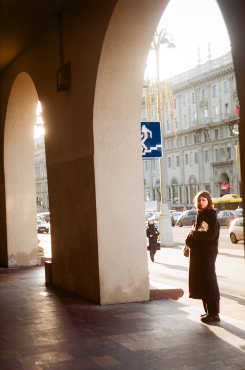 Free A woman stands by an archway in a vibrant city street at sunset. Stock Photo