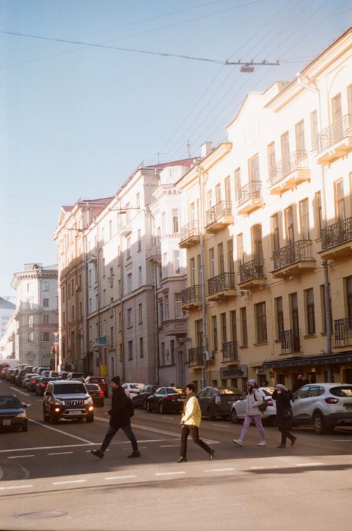 Free A street view of an urban area with pedestrians crossing and historic buildings under sunlight. Stock Photo