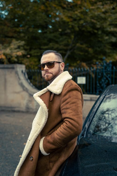 Free Confident man in a brown coat leaning against a car, exuding style and sophistication. Stock Photo