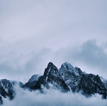 Majestic snowy mountain peaks reach through clouds during an overcast winter day, creating a dramatic and serene landscape.
