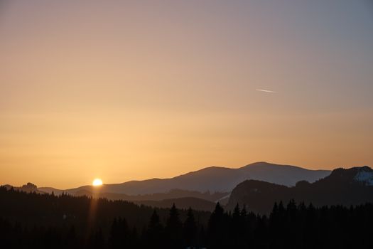 Beautiful sunset over mountains with silhouetted trees and a clear sky.