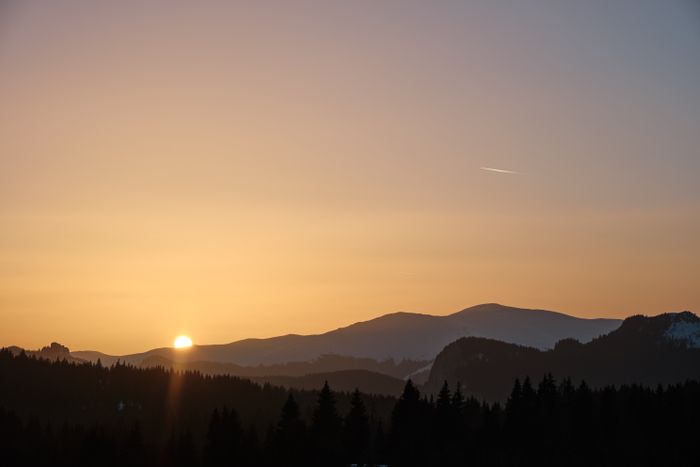 Sunset behind layered ridges and a conifer skyline — photo by Cosmin on Pexels