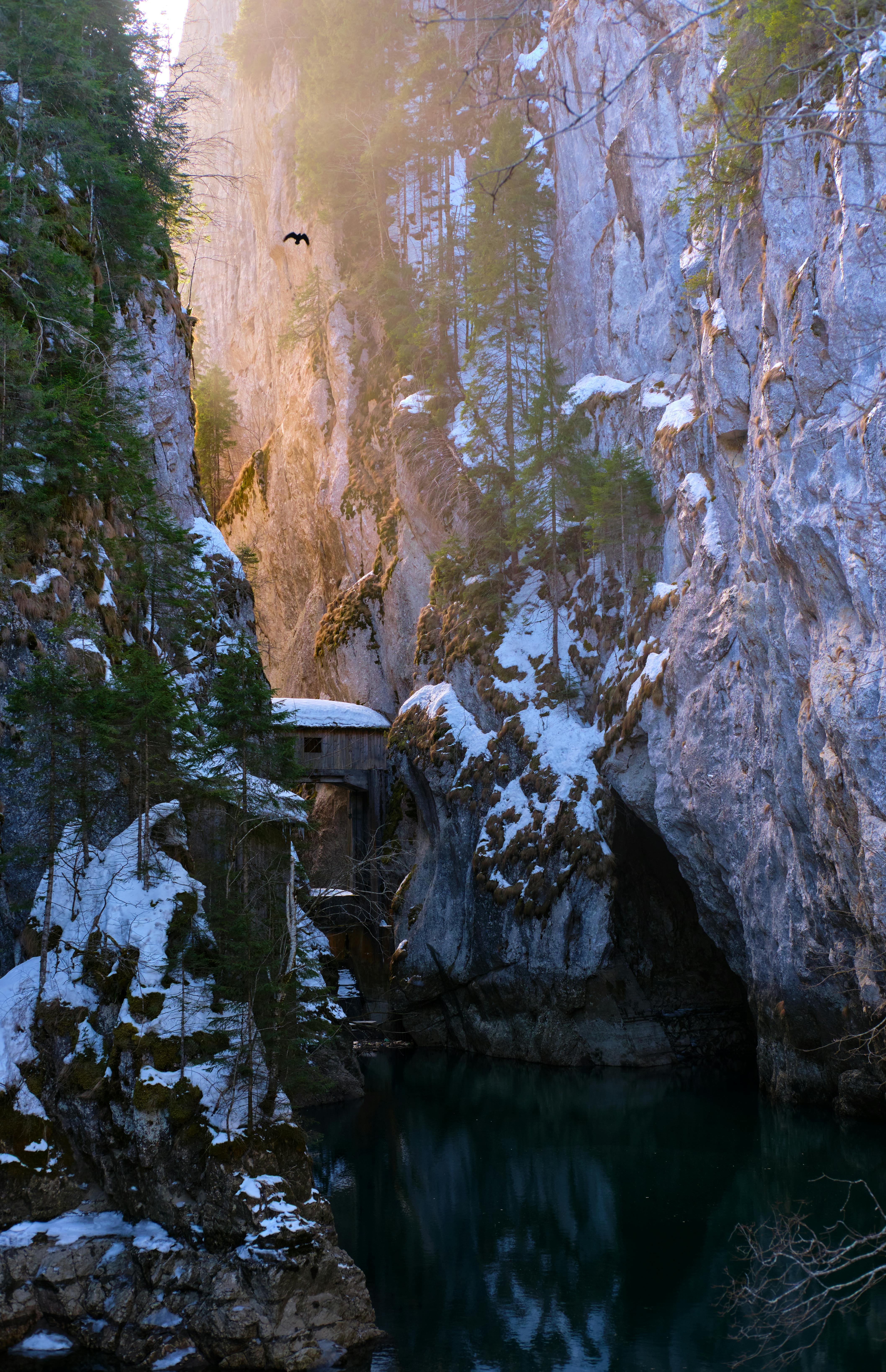 Explore a serene snowy canyon with a hidden cabin and striking water reflection. A winter paradise.