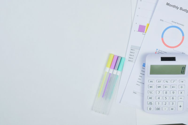 Minimalist office desk with a calculator, budget planning documents, and colorful pens.
