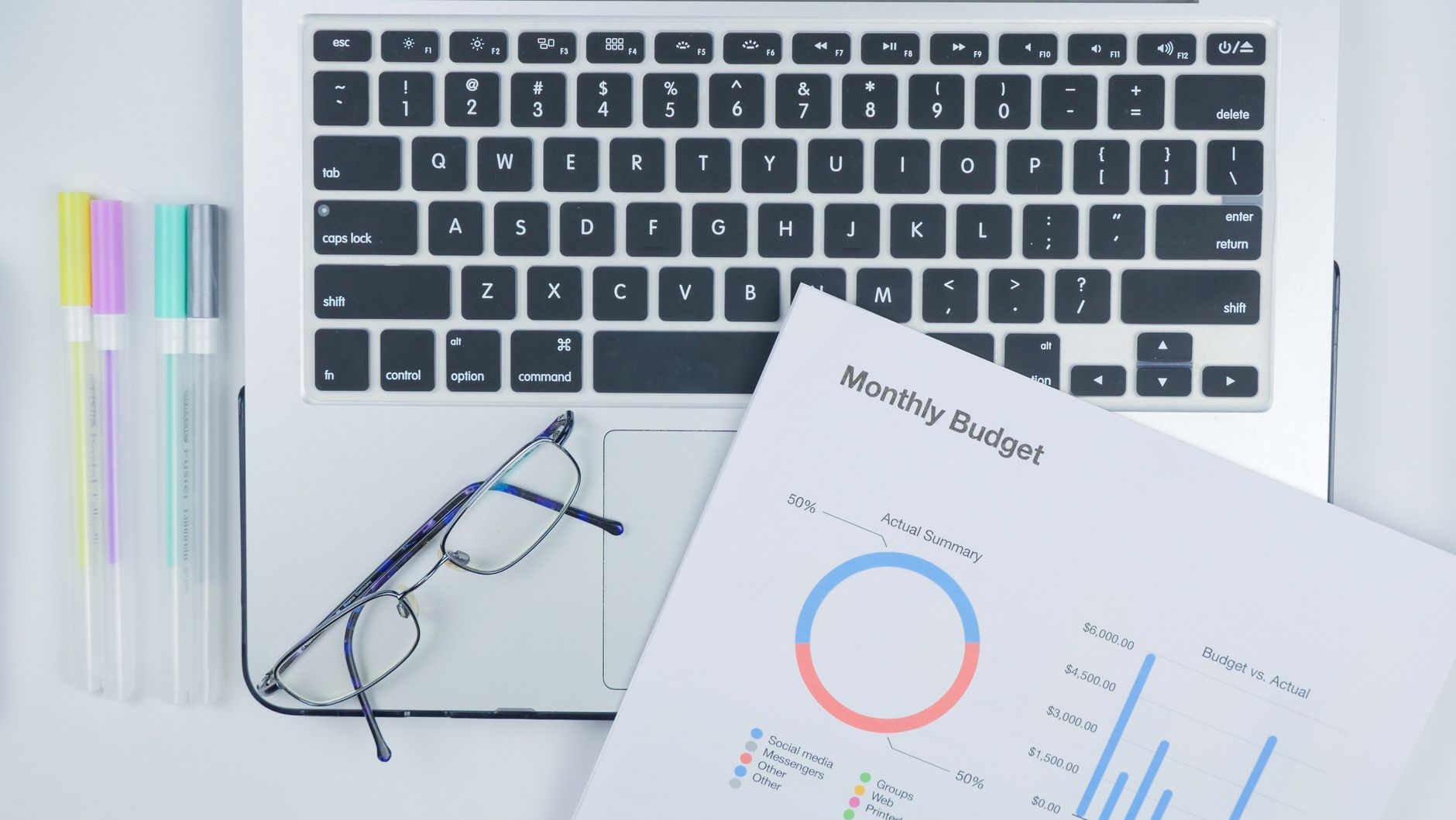 optimalisasi crawl budget - Aerial shot of a modern workspace with a laptop, budget report, and eyeglasses on a desk.