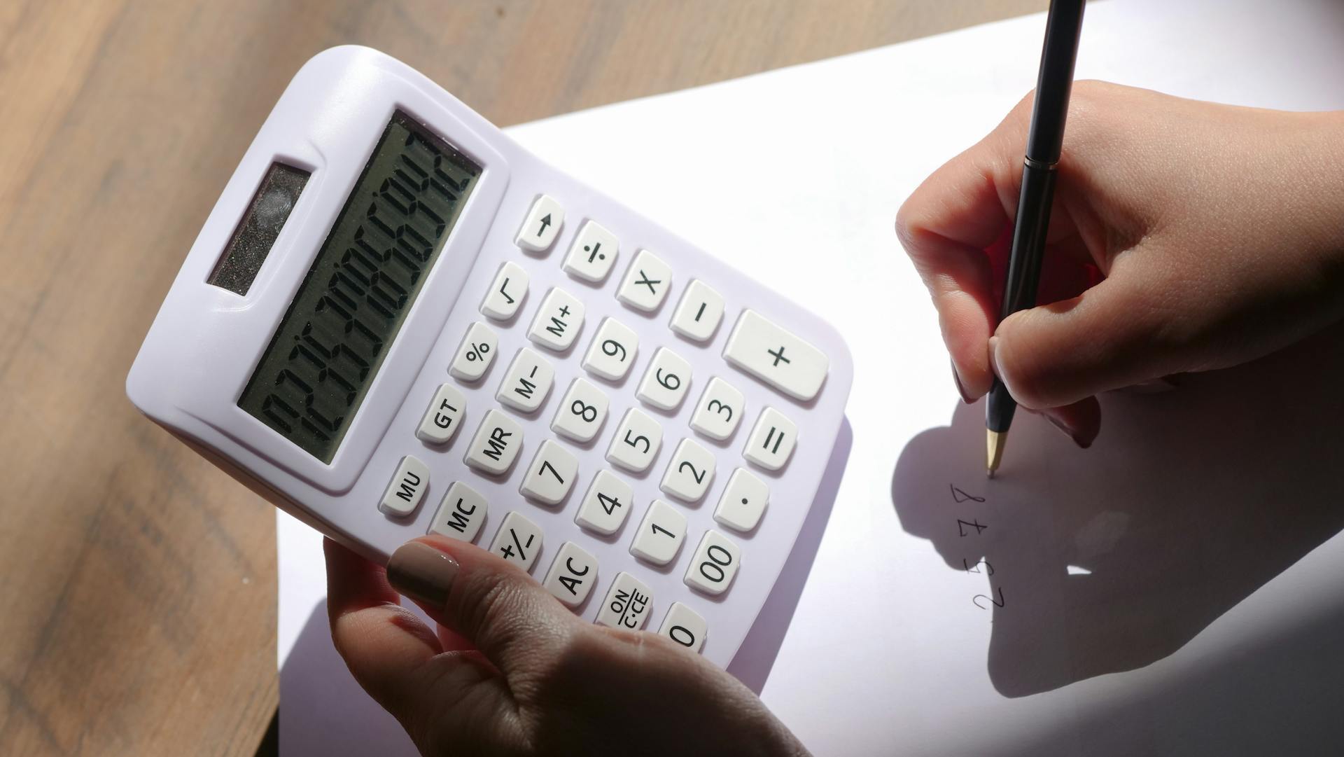 Close-up of hands holding a calculator and writing on paper, depicting calculation and analysis.