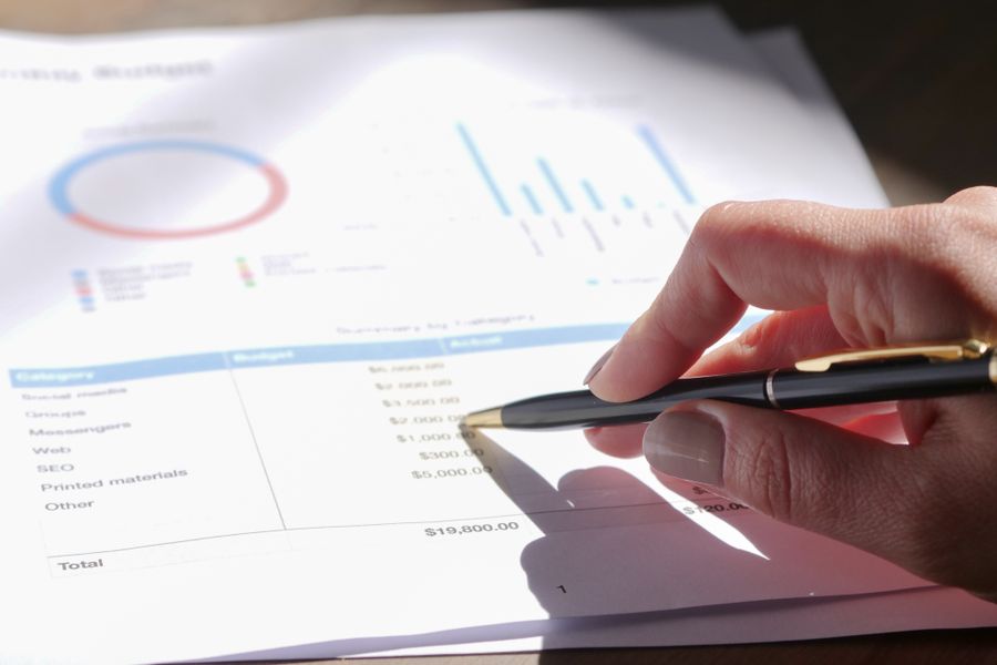 Hand holding pen, analyzing budget with charts and graph paper.