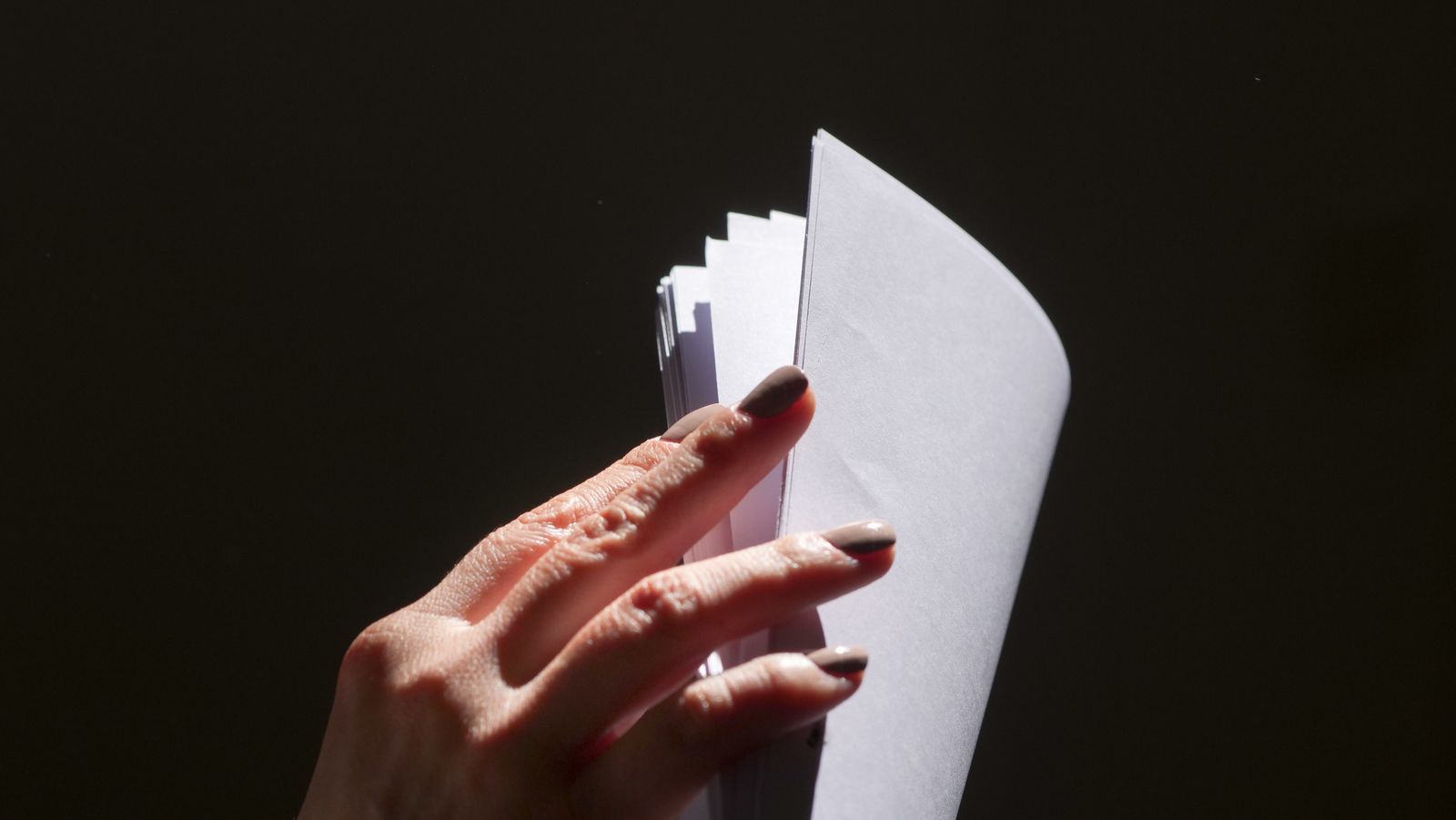 Close-up of a hand flipping through a stack of paper documents