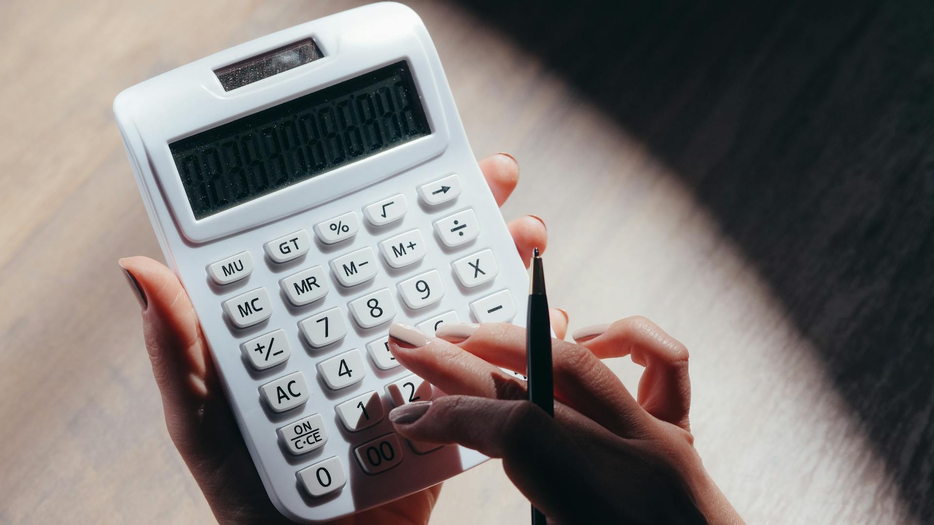 Hands holding a calculator and pen for financial calculations in a well-lit setting.