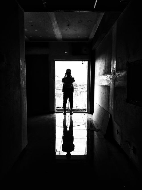Free A monochrome silhouette of a person standing in a doorway with reflective floors. Stock Photo